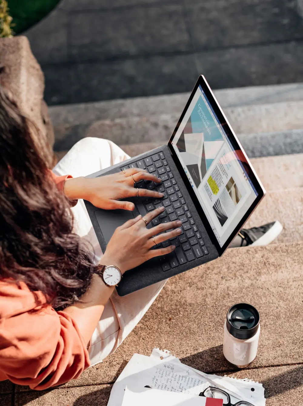 Vrouw typt op een laptop, buiten op een trap